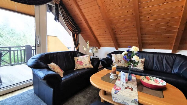 Ein gemütliches Zimmer mit einer schwarzen Ledersofa, einem Holztisch und Blick ins Freie.