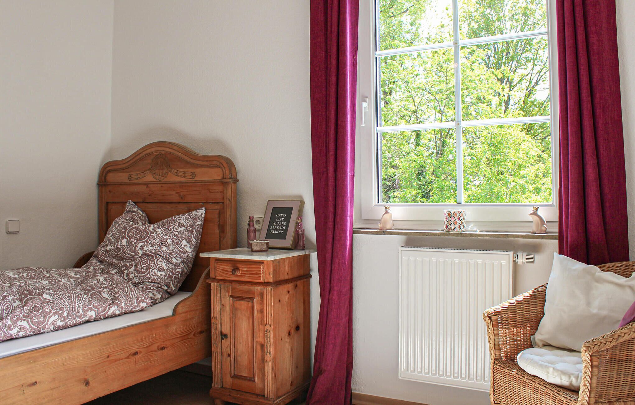 A bedroom with a wooden bed, a nightstand, a wicker chair, and a window with curtains.