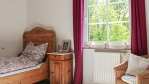 Une chambre à coucher avec un lit en bois, une table de chevet, une chaise en osier et une fenêtre avec des rideaux.