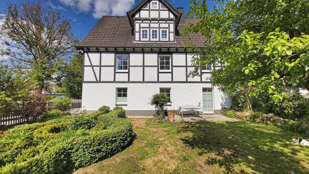 Une maison à deux étages, dotée d’un toit à forte pente, de lucarnes et d’une façade symétrique.