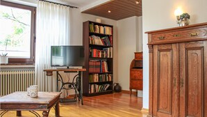 Un salon comprenant un téléviseur, une bibliothèque, un meuble en bois et une table avec deux chaises.