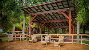 Une terrasse en bois avec des chaises longues, une piscine et un pavillon abrité.