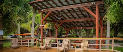 Eine Holzterrasse mit Liegestühlen, einem Pool und einem überdachten Pavillon.