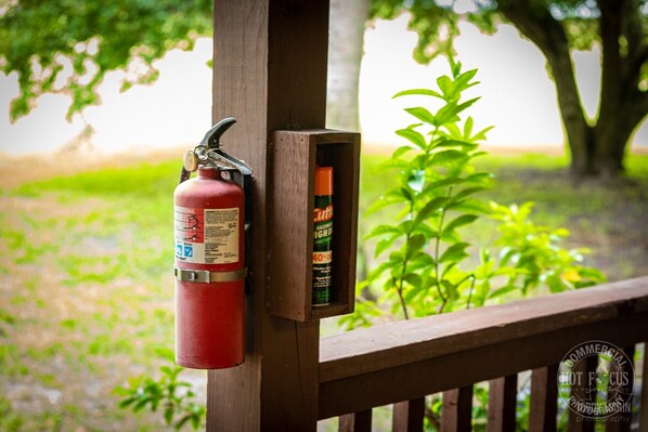 A fire extinguisher mounted on a wooden railing with a small box containing a spray bottle. - Quaint rustic cabin, newly remodeled! (Clewiston)