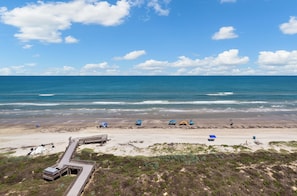 A beach with a wooden boardwalk, tents, and a clear blue sky.