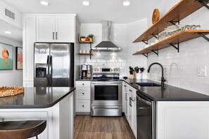 A modern kitchen with white cabinets, stainless steel appliances, and wooden shelves.