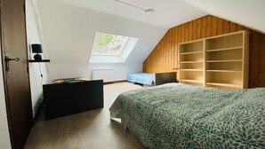 Een slaapkamer met een schuine kap, dakraam, een bed met een bedsprei met patroon, een houten garderobe en een bureau met lamp.