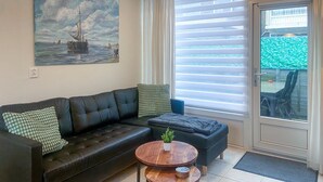 Una sala de estar con un sofá de cuero negro, dos sillones a juego, una mesa de centro de madera y un cuadro de un barco velero en la pared.