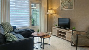 Una sala de estar moderna con un sofá, una mesa de centro, un televisor sobre un mueble de madera y un cuadro en la pared.