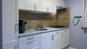 Una cocina moderna con armarios blancos, un lavamanos de acero inoxidable, una estufa a gas y una cafetera.