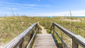 Een houten looppad dat naar een strand leidt, met een tent in de verte.