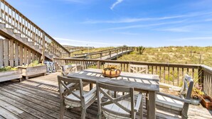 Een houten terras met een tafel en stoelen, omgeven door een houten balustrade, met uitzicht op een grasveld.