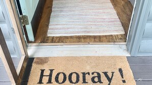 Un pavimento in legno, un tappeto a righe e un tappetino d'ingresso con la scritta 'Hooray! you're here'.