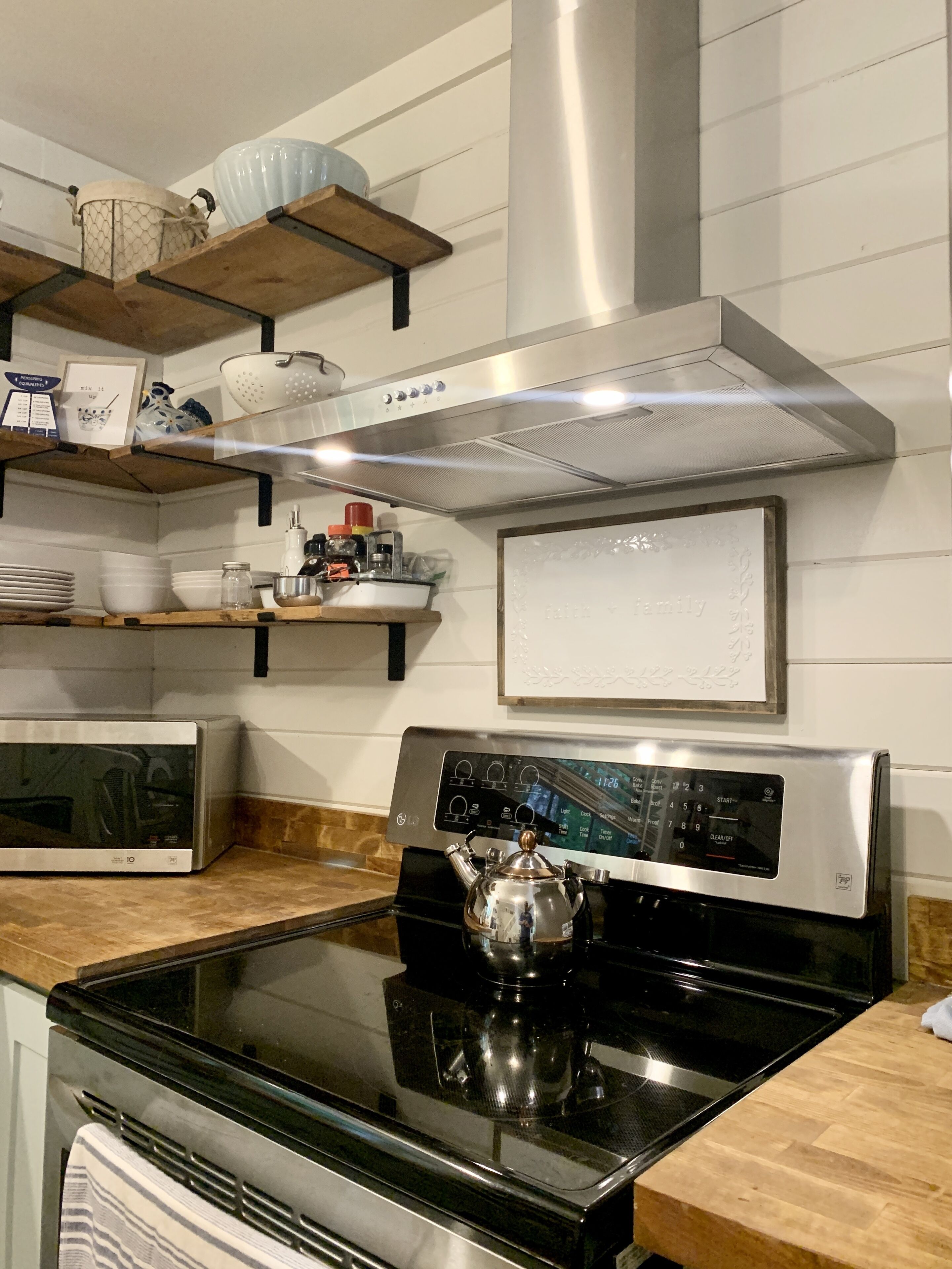 Une cuisine moderne dotée d’appareils électroménagers en acier inoxydable, d’étagères en bois et d’une théière décorative.