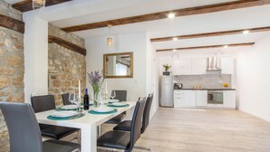 A dining area with a stone wall, a wooden ceiling, and a kitchen in the background.
