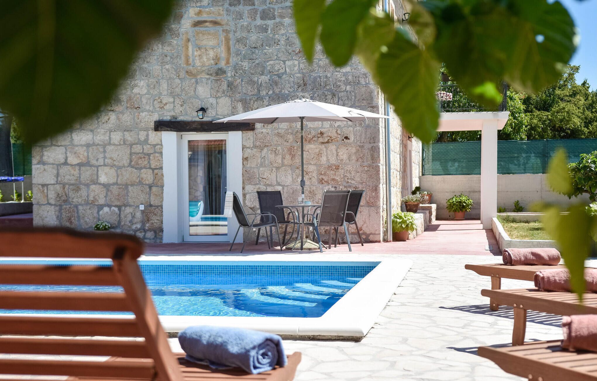 A pool area with a stone building, outdoor seating, and a covered patio.