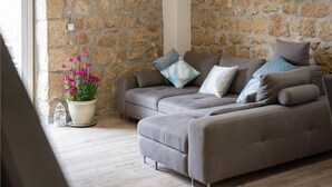 A modern living room with a stone wall, a grey sofa, and a potted plant with pink flowers.