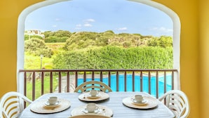 Varanda com mesa posta para quatro pessoas, vista para uma piscina e vegetação exuberante.