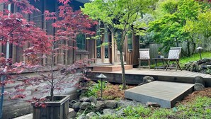 A wooden house with a deck, surrounded by trees with red and green leaves. - The Bathhouse: Boho Modern + Hot Tub + Water View (Mill Valley)