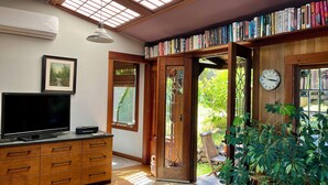 A room with a skylight, a bookshelf, a TV, and a wooden cabinet. - The Bathhouse: Boho Modern + Hot Tub + Water View (Mill Valley)