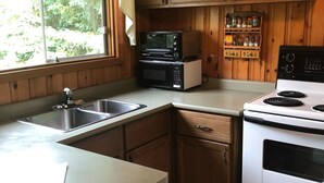 A kitchen with wooden cabinets, a sink, a microwave, a stove, and a window with a view of greenery. - Single Family Cottage Perfect for Families with Kids Charm and Sunset Included (McKellar)