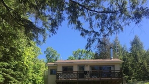 A two-story house with a balcony, surrounded by trees and a grassy yard. - Single Family Cottage Perfect for Families with Kids Charm and Sunset Included (McKellar)