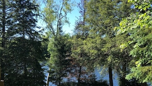 A natural landscape with a variety of trees, a grassy area, and a body of water in the background. - Single Family Cottage Perfect for Families with Kids Charm and Sunset Included (McKellar)