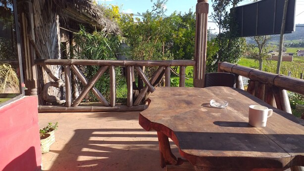An outdoor wooden deck with a table and chairs, surrounded by bamboo fencing and greenery.