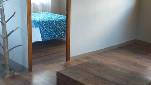 A room with a wooden floor, a bed with a blue floral bedspread, a wooden chest of drawers, and a small tree decoration.