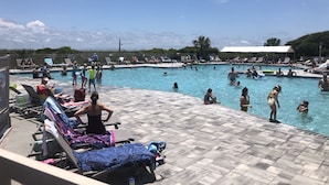 A swimming pool with people in and around it, lounge chairs, and a covered area.