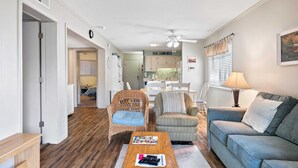 A living room with a wooden floor, a ceiling fan, a sofa, a coffee table, and a dining area with a table and chairs.