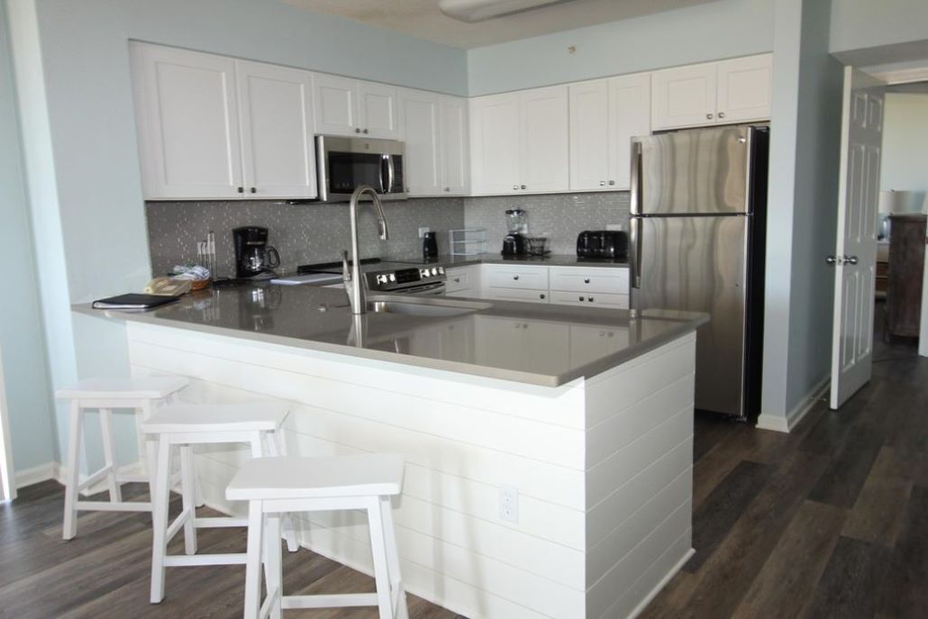 A modern kitchen with white cabinetry, stainless steel appliances, and a central island with stools.
