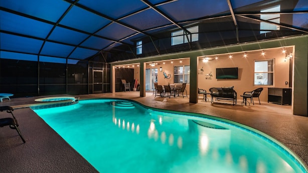 Une piscine intérieure dotée d’un patio couvert, de sièges et d’un téléviseur.