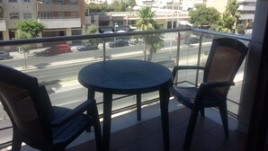 A balcony with a round table and two chairs, overlooking a street with cars and buildings. - Paseo Marítimo Antonio Banderas (Málaga)