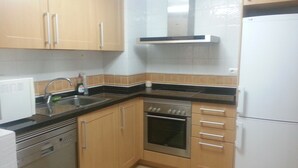 A compact kitchen with wooden cabinets, a stainless steel oven, a white refrigerator, and a black countertop. - Paseo Marítimo Antonio Banderas (Málaga)