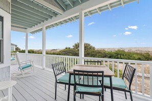 A covered outdoor area with a table and chairs, a rocking chair, and a view of the landscape. - Inn Denial - Unmatched Oceanfront Elegance! (Bald Head Island)
