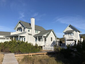 Una casa costanera amb un terrat de fusta, una xemeneia gran i una tanca blanca.