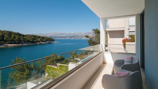 Een balkon met vrij uitzicht op een kustlandschap, inclusief een waterpartij en verre bergen.