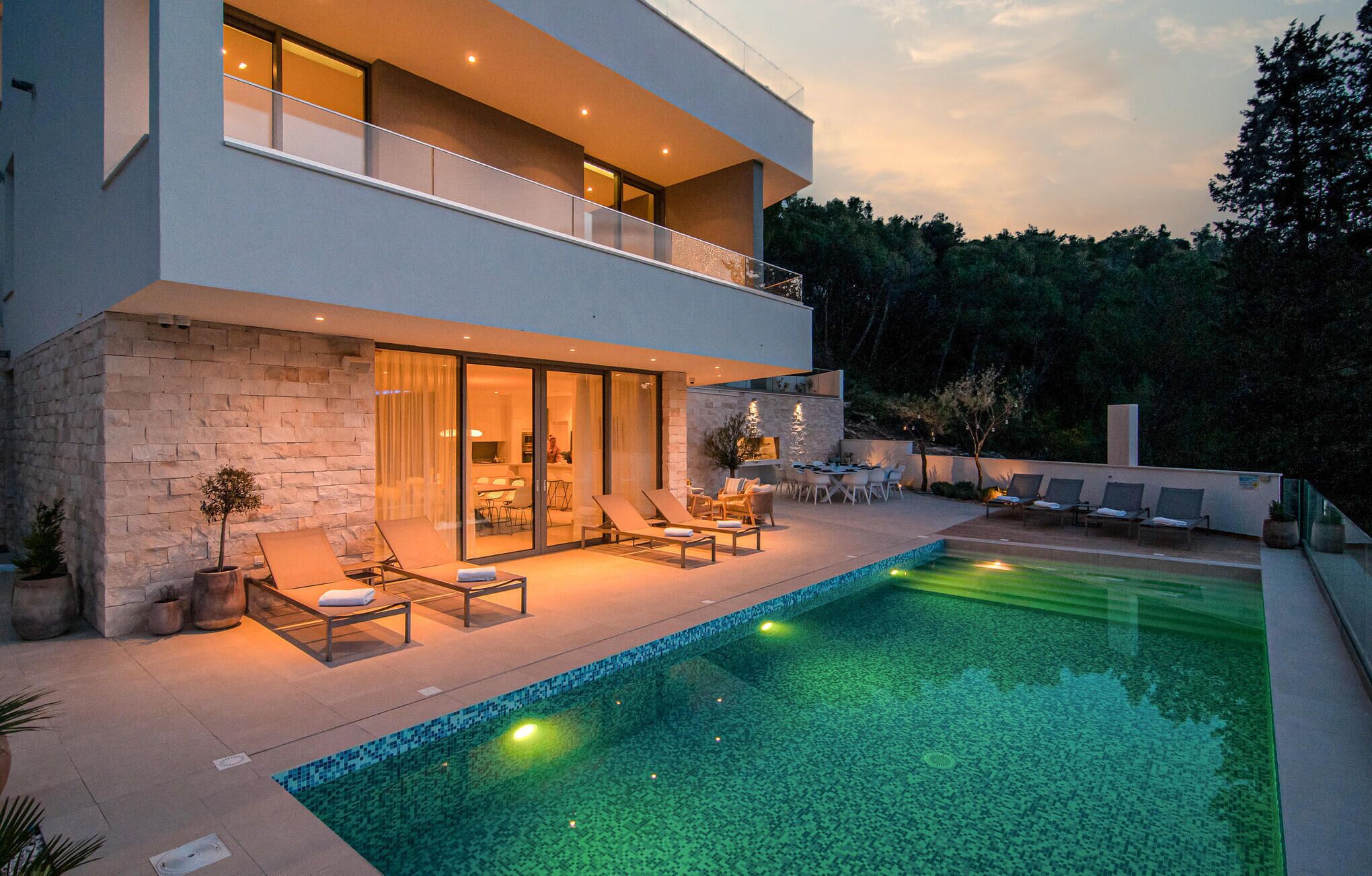A modern two-story house with a swimming pool, outdoor seating, and a stone facade.