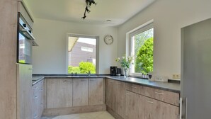 A modern kitchen with light wood cabinets, a stainless steel refrigerator, a coffee maker, and a clock on the wall.