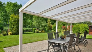 A covered patio area with a table and chairs, surrounded by a well-maintained garden.