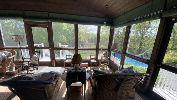 Une véranda meublée de mobilier en osier, avec une table et des chaises, donnant sur une piscine et une végétation luxuriante.
