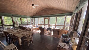 Une pièce spacieuse avec un plafond en bois, de grandes fenêtres et un coin repas comprenant une table et des chaises.