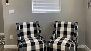 A room with two checkered armchairs, a window with blinds, a power outlet, and a decorative plant. - Home on the Range (Hurricane)