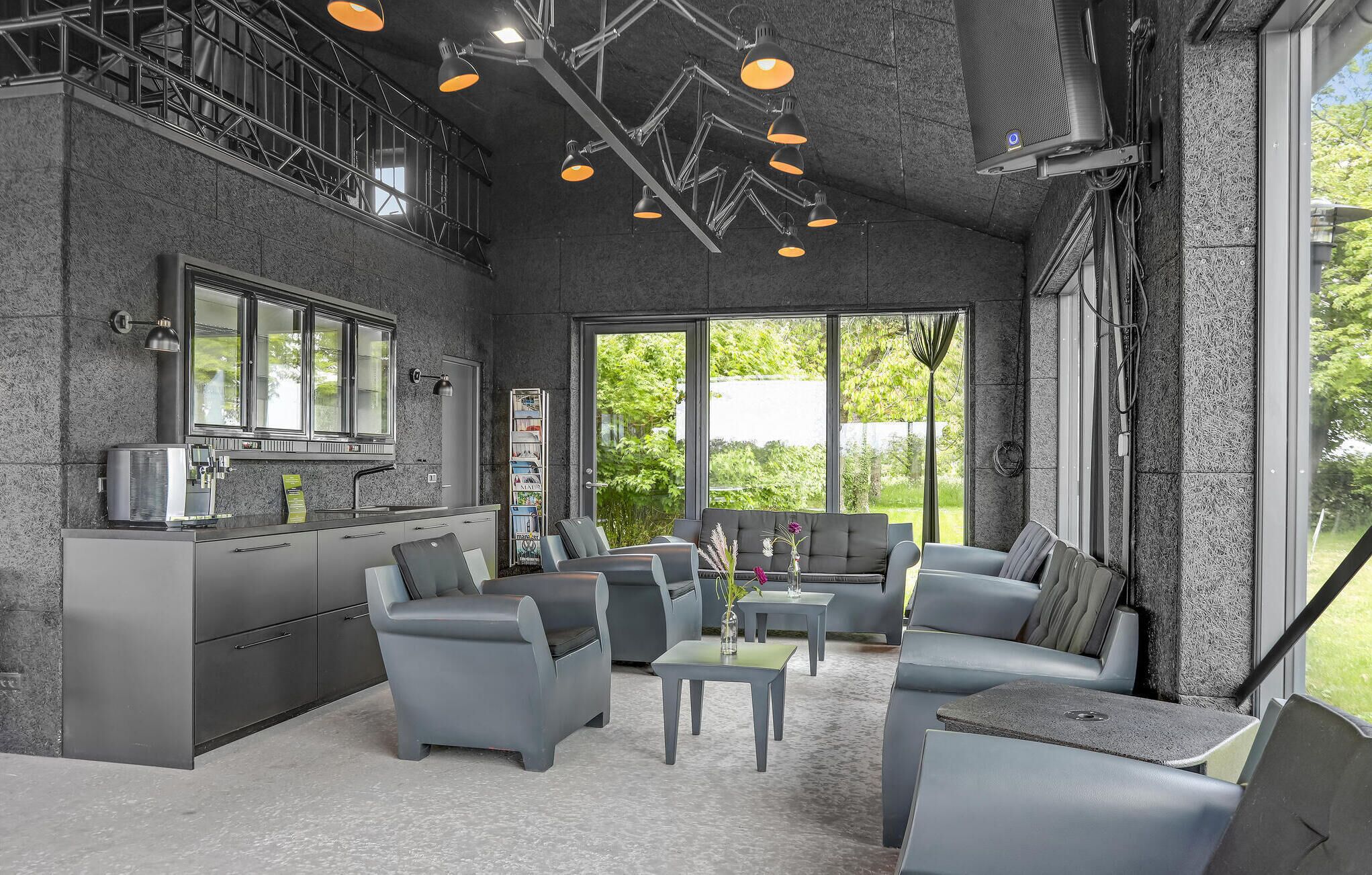 A modern kitchen with a built-in stove, a dining area with grey upholstered chairs, and large windows offering a view of greenery.
