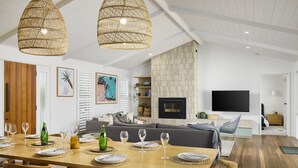 Una sala de estar moderna con comedor, que incluye una chimenea, un televisor de pantalla plana y lámparas colgantes de mimbre.