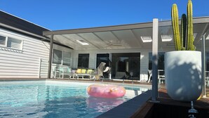 Una piscina con cerramiento de vidrio, un cactus y mobiliario de exterior.