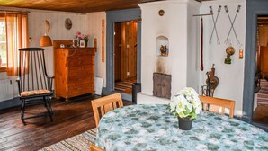 Una habitación acogedora con piso de madera, una mesa redonda con mantel floral, una silla de madera, un aparador y una chimenea.