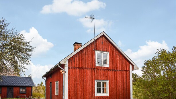 Una casa de madera roja con techo inclinado, una chimenea y un ventanal pequeño.