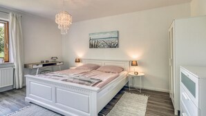 Ein Schlafzimmer mit Bett, Nachttischlampen, Schreibtisch, Heizkörper und einem Bild an der Wand.